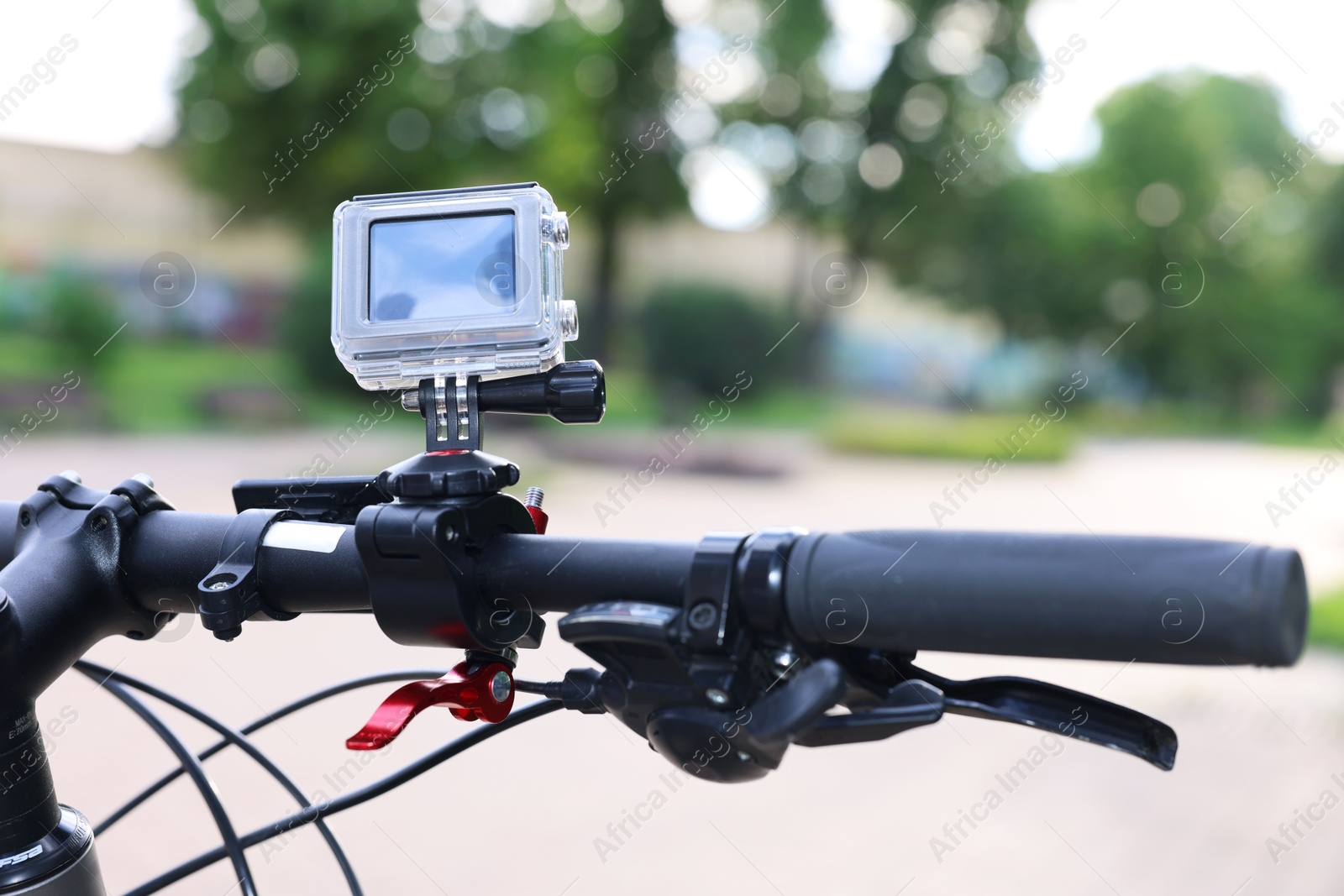 Photo of Modern action camera with mount on bicycle outdoors, closeup