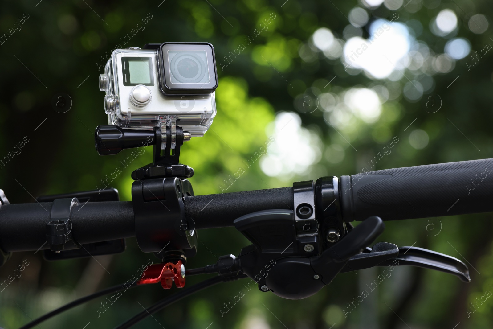 Photo of Modern action camera with mount on bicycle outdoors, closeup