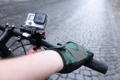 Photo of Man riding bicycle with modern action camera outdoors, closeup