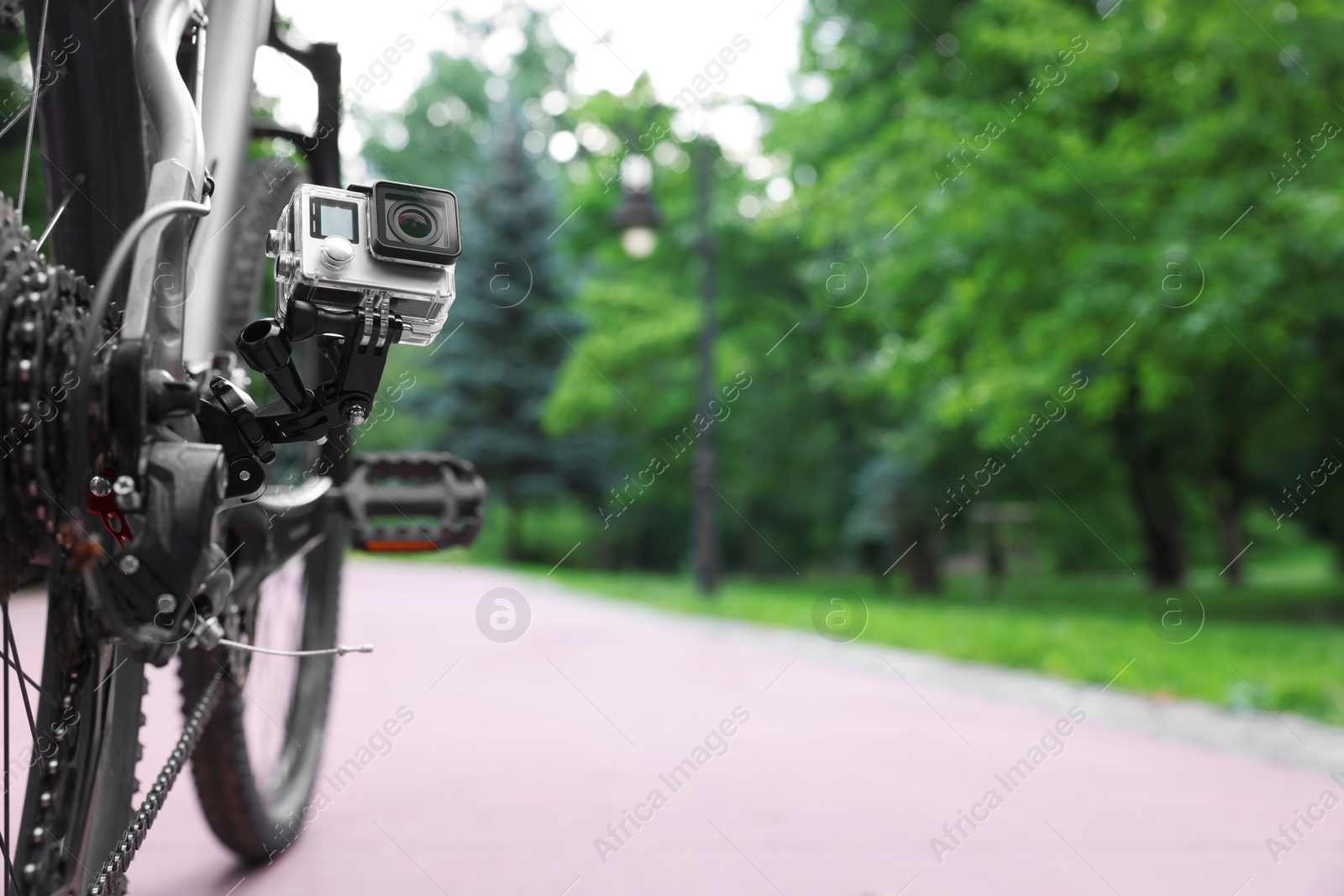 Photo of Modern action camera with mount on bicycle outdoors. Space for text