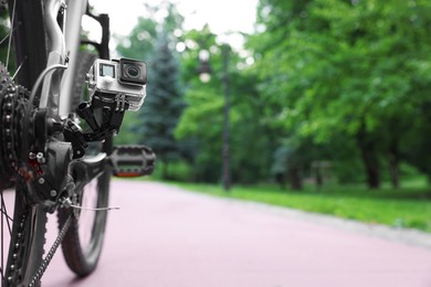 Photo of Modern action camera with mount on bicycle outdoors. Space for text