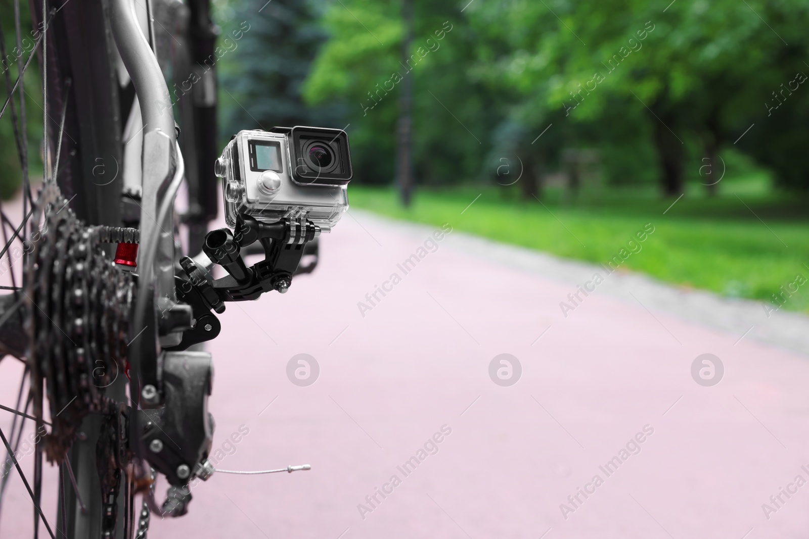 Photo of Modern action camera with mount on bicycle outdoors. Space for text