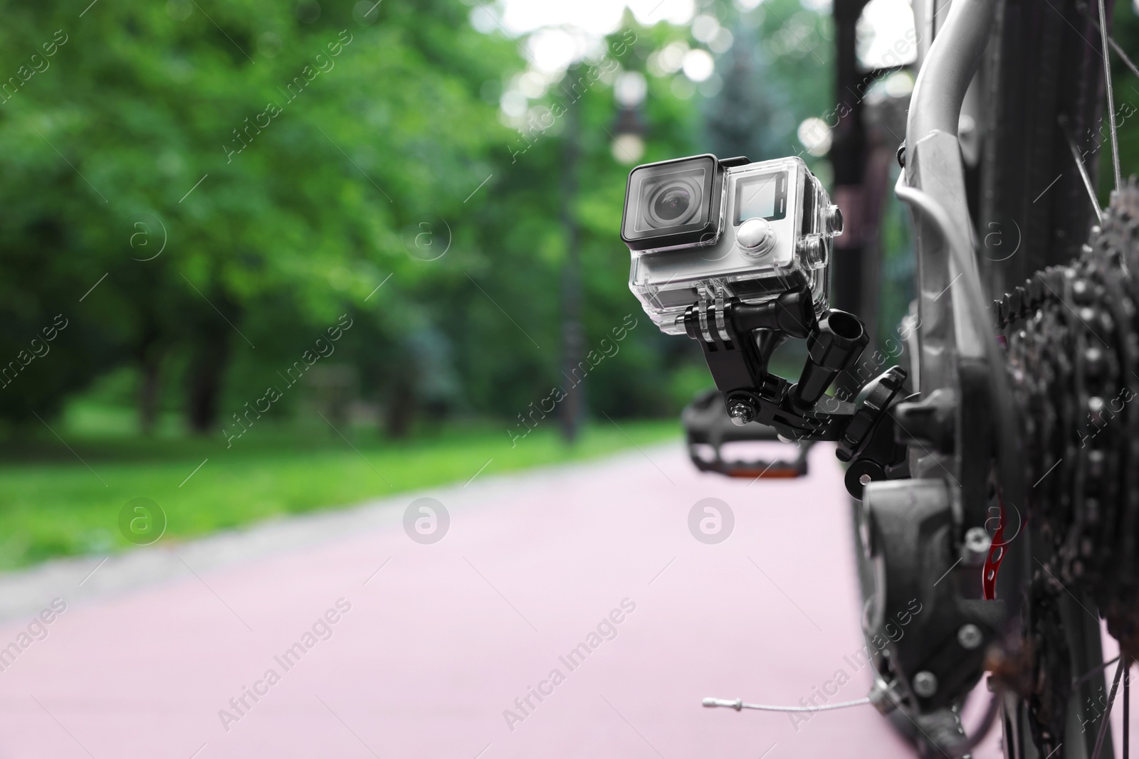 Photo of Modern action camera with mount on bicycle outdoors. Space for text