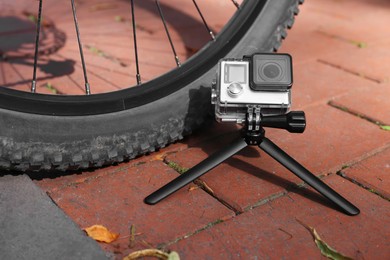 Modern action camera with tripod near bicycle outdoors