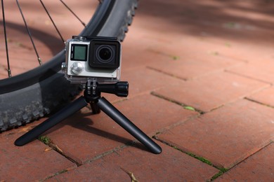 Modern action camera with tripod near bicycle outdoors. Space for text