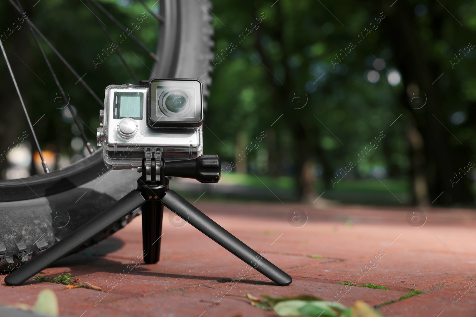 Photo of Modern action camera with tripod near bicycle outdoors. Space for text