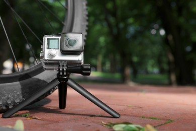 Modern action camera with tripod near bicycle outdoors. Space for text