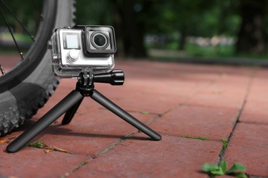 Modern action camera with tripod near bicycle outdoors. Space for text