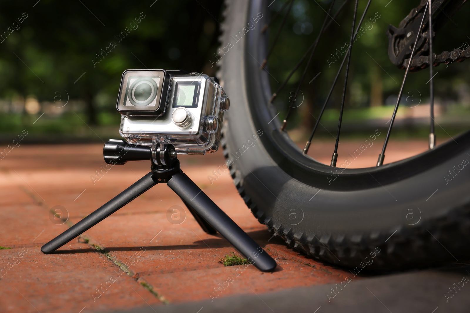 Photo of Modern action camera with tripod near bicycle outdoors