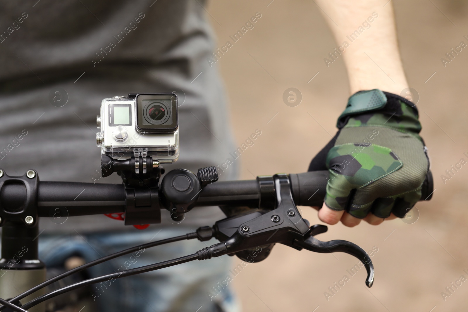 Photo of Man riding bicycle with modern action camera outdoors, closeup