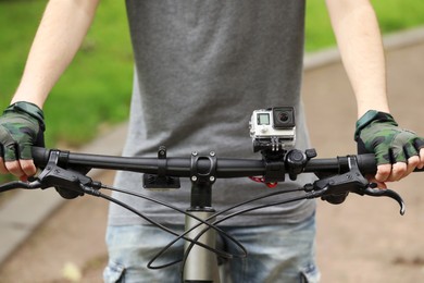 Photo of Man riding bicycle with modern action camera outdoors, closeup