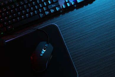 Photo of Computer mouse, mousepad and keyboard on dark wooden table in neon lights, flat lay. Space for text