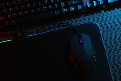 Photo of Computer mouse, mousepad and keyboard on dark wooden table in neon lights, flat lay