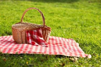 Photo of One picnic wicker basket with checkered napkin and blanket on green grass. Space for text