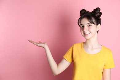 Portrait of smiling teenage girl holding something on pink background. Space for text