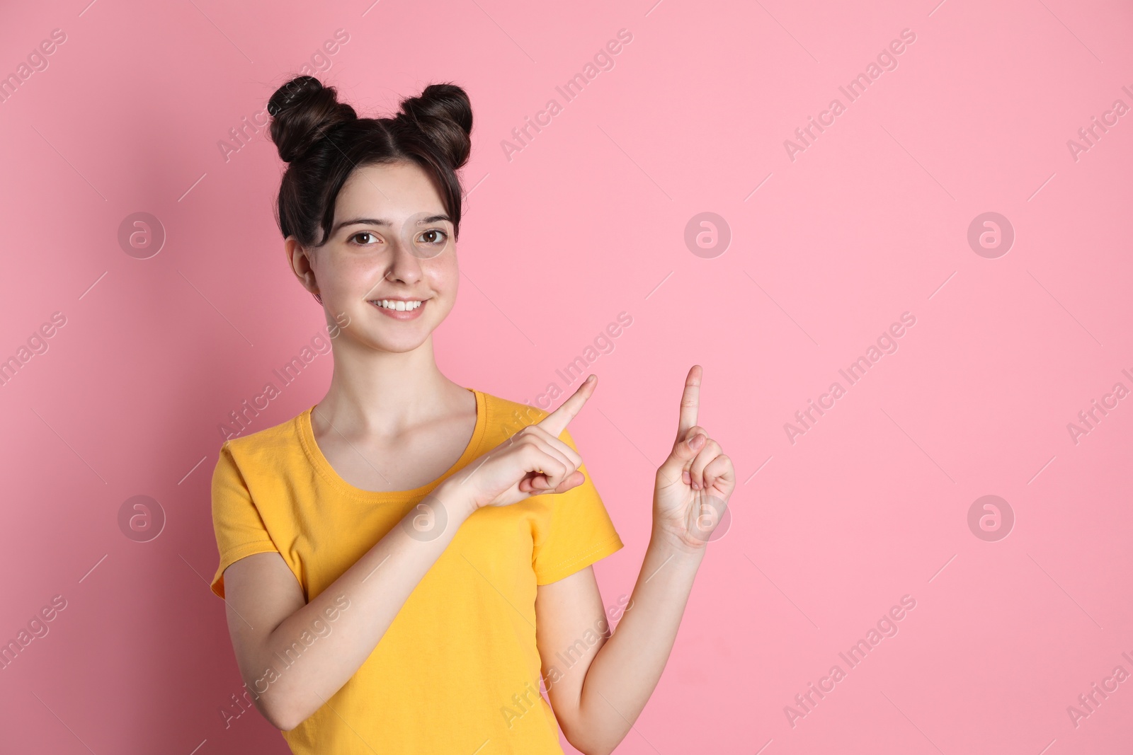 Photo of Portrait of smiling teenage girl pointing at something on pink background. Space for text