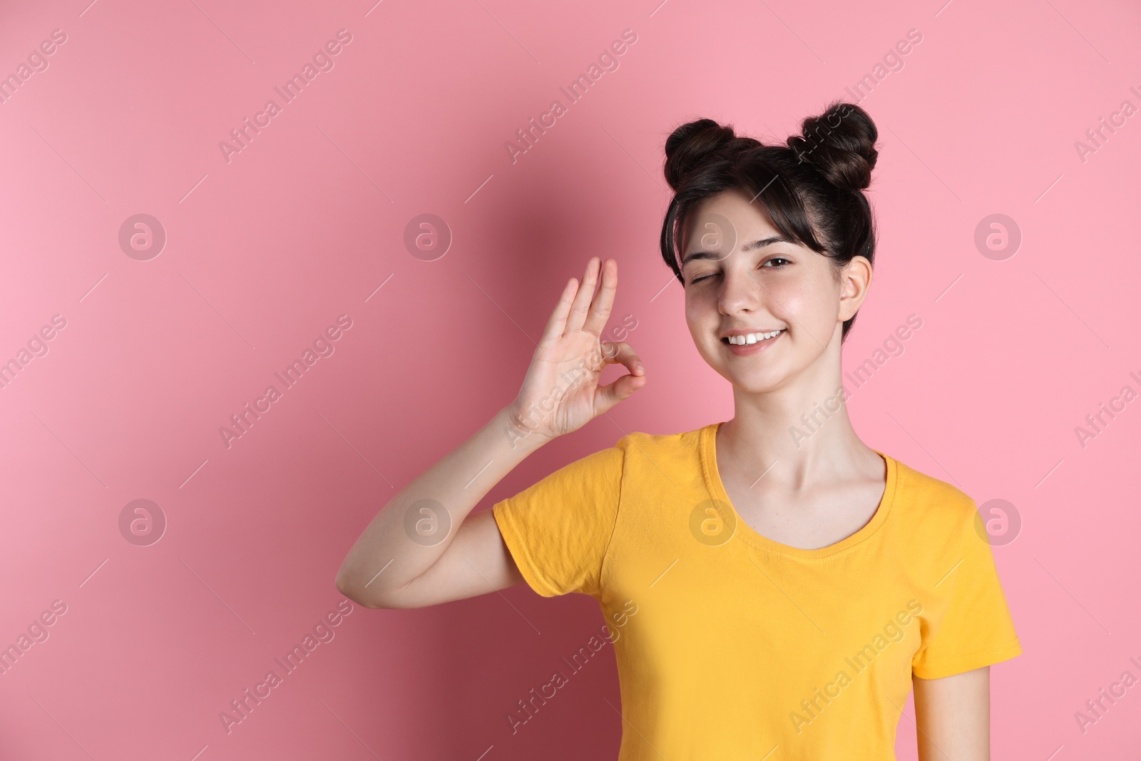 Photo of Portrait of smiling teenage girl showing ok gesture on pink background. Space for text