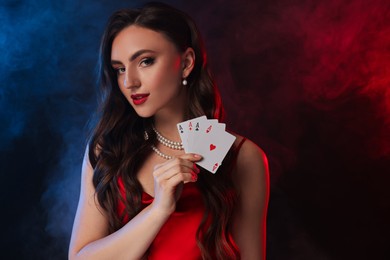 Poker game. Charming woman with playing cards on black background in color lights and smoke