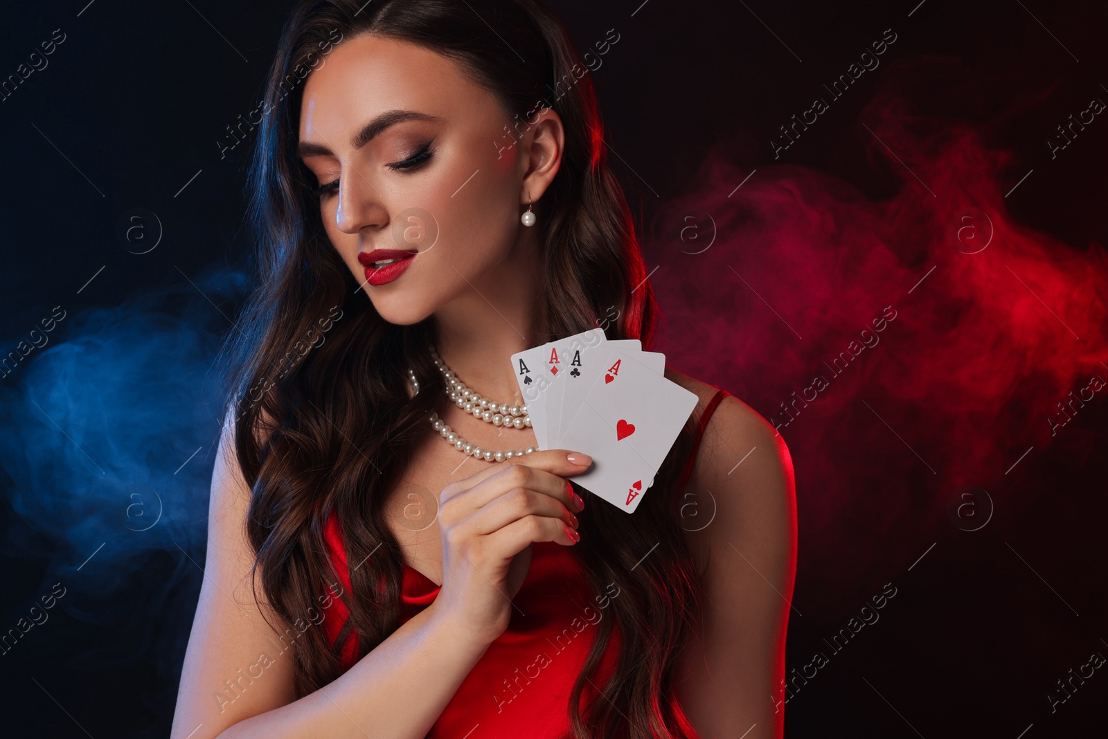 Photo of Poker game. Charming woman with playing cards on black background in color lights and smoke