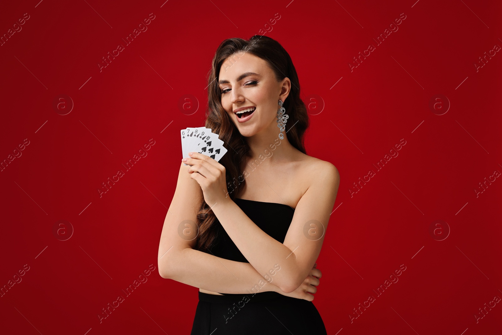 Photo of Poker game. Happy woman with playing cards on red background