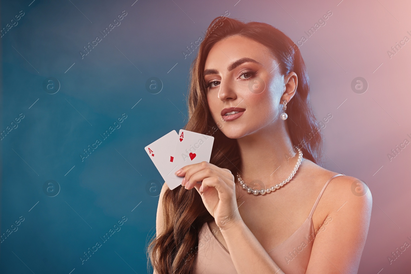 Photo of Poker game. Charming woman holding playing cards on light blue background with smoke. Space for text