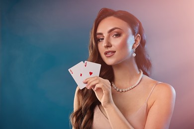 Poker game. Charming woman holding playing cards on light blue background with smoke. Space for text