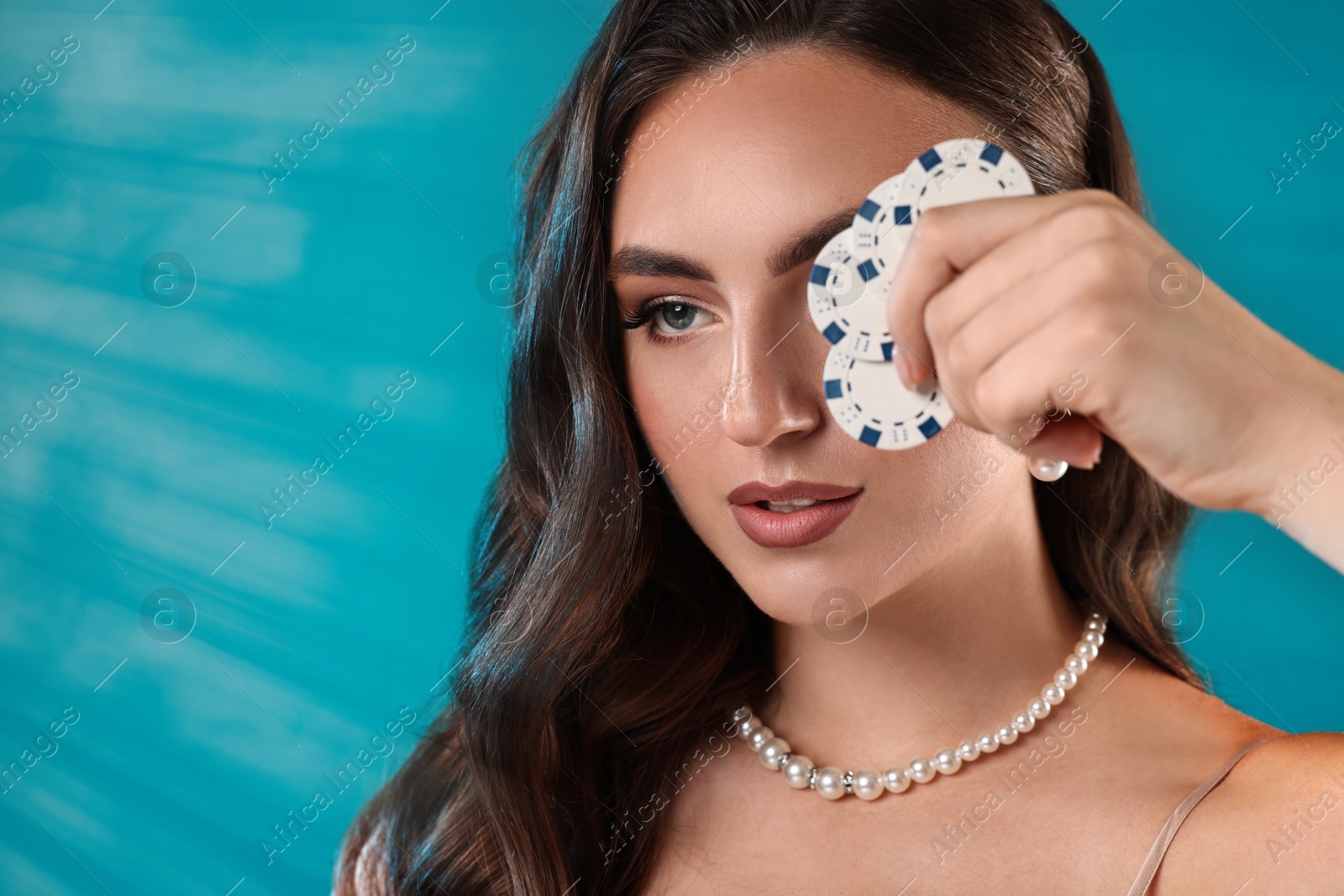 Photo of Charming woman covering eye with poker chips on light blue background. Space for text