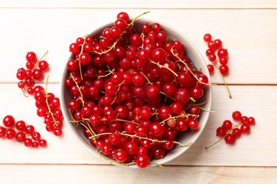 Fresh red currant berries in bowl on white wooden table, top view