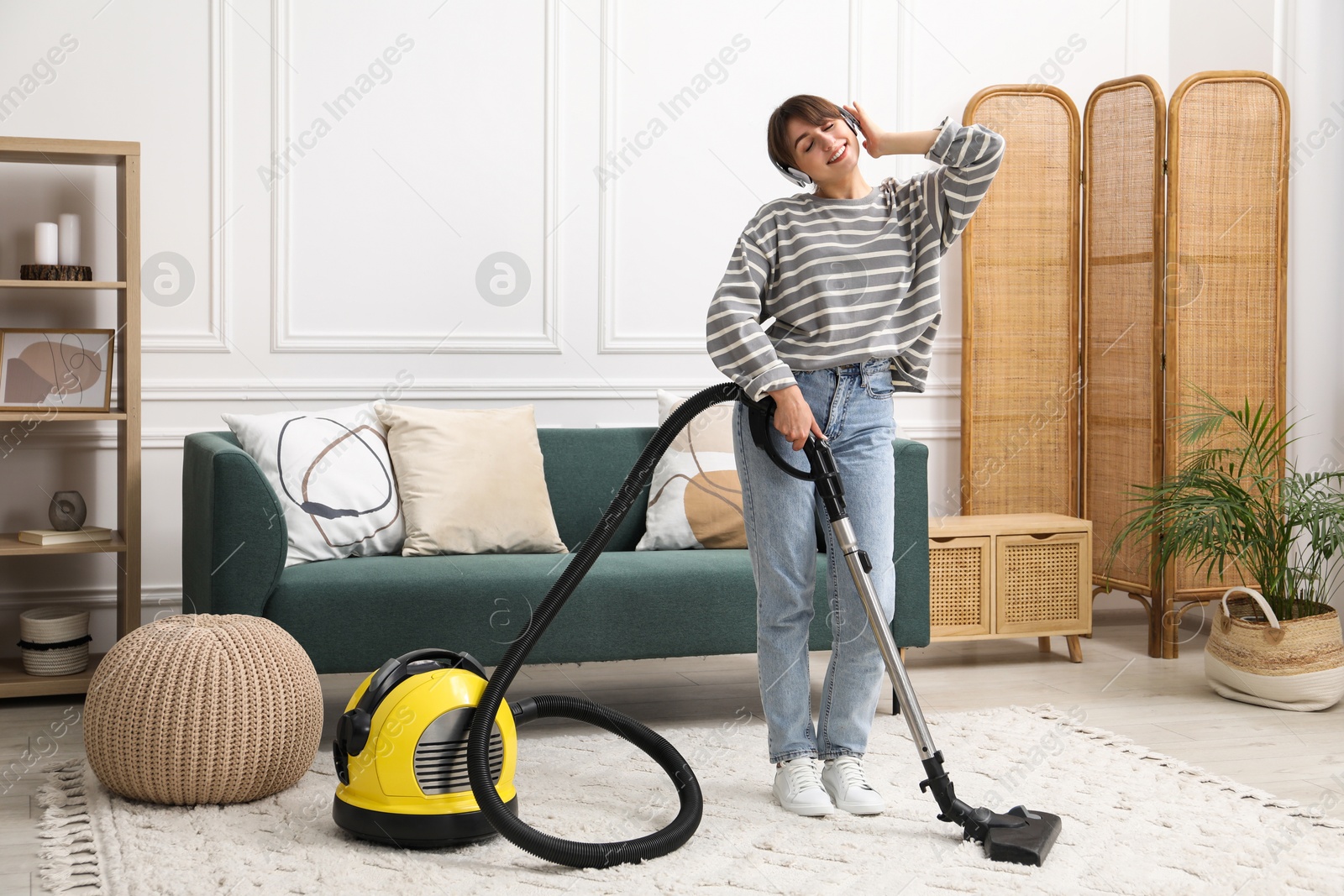 Photo of Young woman wearing headphones cleaning carpet with vacuum in living room