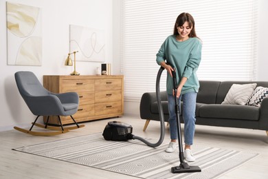 Photo of Young woman vacuuming carpet in living room