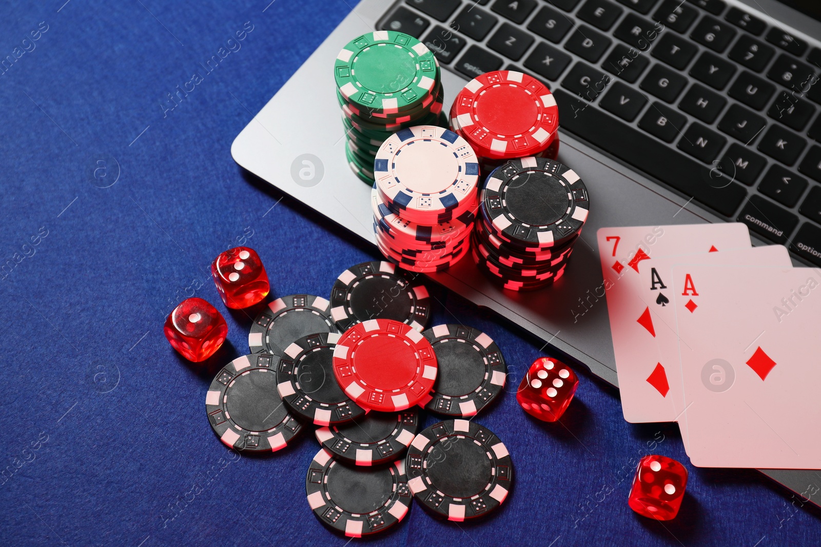 Photo of Poker chips, laptop, playing cards and dices on blue table, above view. Online game