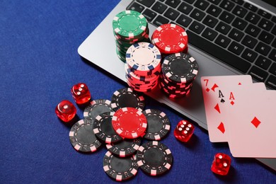 Photo of Poker chips, laptop, playing cards and dices on blue table, above view. Online game