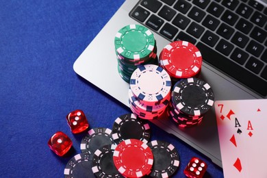 Photo of Poker chips, laptop, playing cards and dices on blue table, above view. Online game