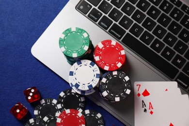 Photo of Poker chips, laptop, playing cards and dices on blue table, flat lay. Online game