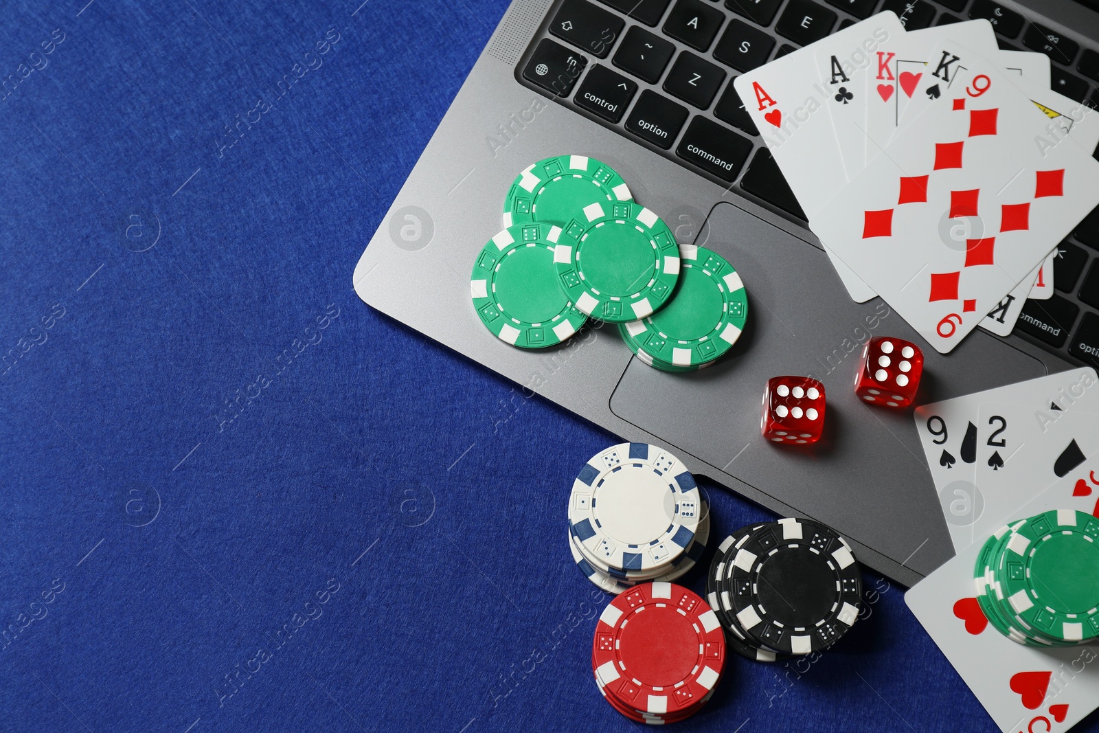 Photo of Online game. Poker chips, laptop, playing cards and dices on blue table, flat lay. Space for text