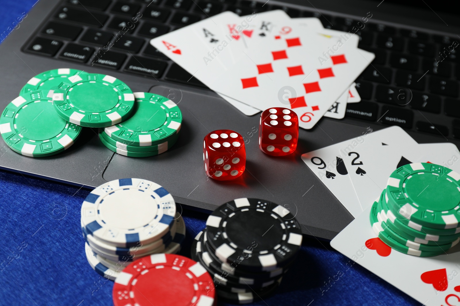 Photo of Poker chips, laptop, playing cards and dices on blue table. Online game