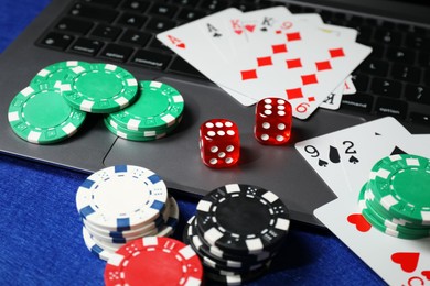 Photo of Poker chips, laptop, playing cards and dices on blue table. Online game