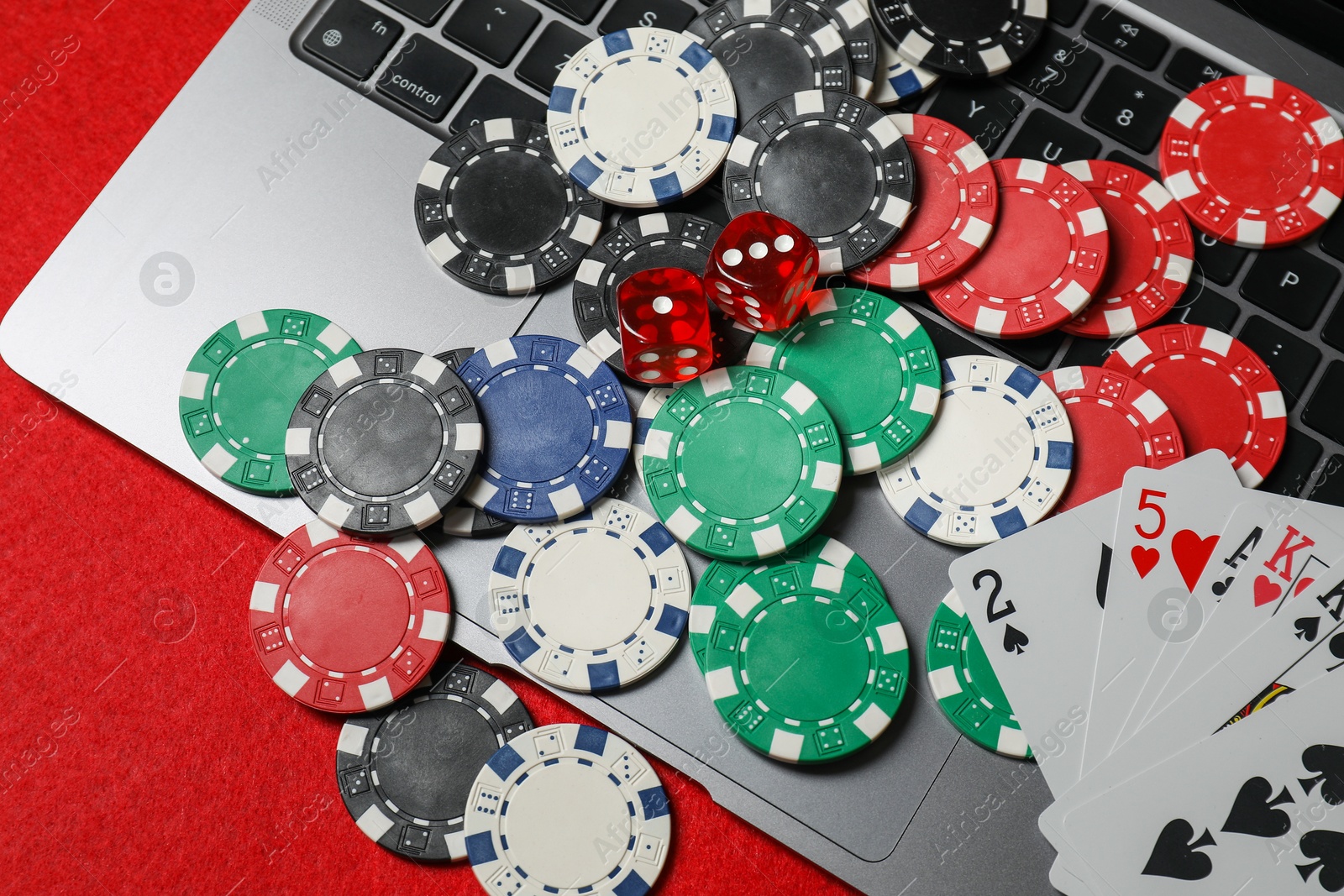 Photo of Poker chips, laptop, playing cards and dices on red table, flat lay. Online game