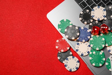 Online game. Poker chips, laptop and dices on red table, flat lay. Space for text