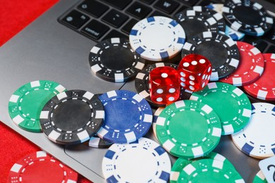 Poker chips, laptop and dices on red table, closeup. Online game