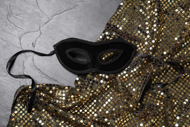 Beautiful carnival mask and fabric with golden sequins on grey textured background, top view