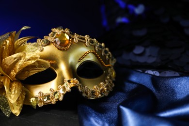 Beautiful golden carnival mask on blue fabric in darkness, closeup