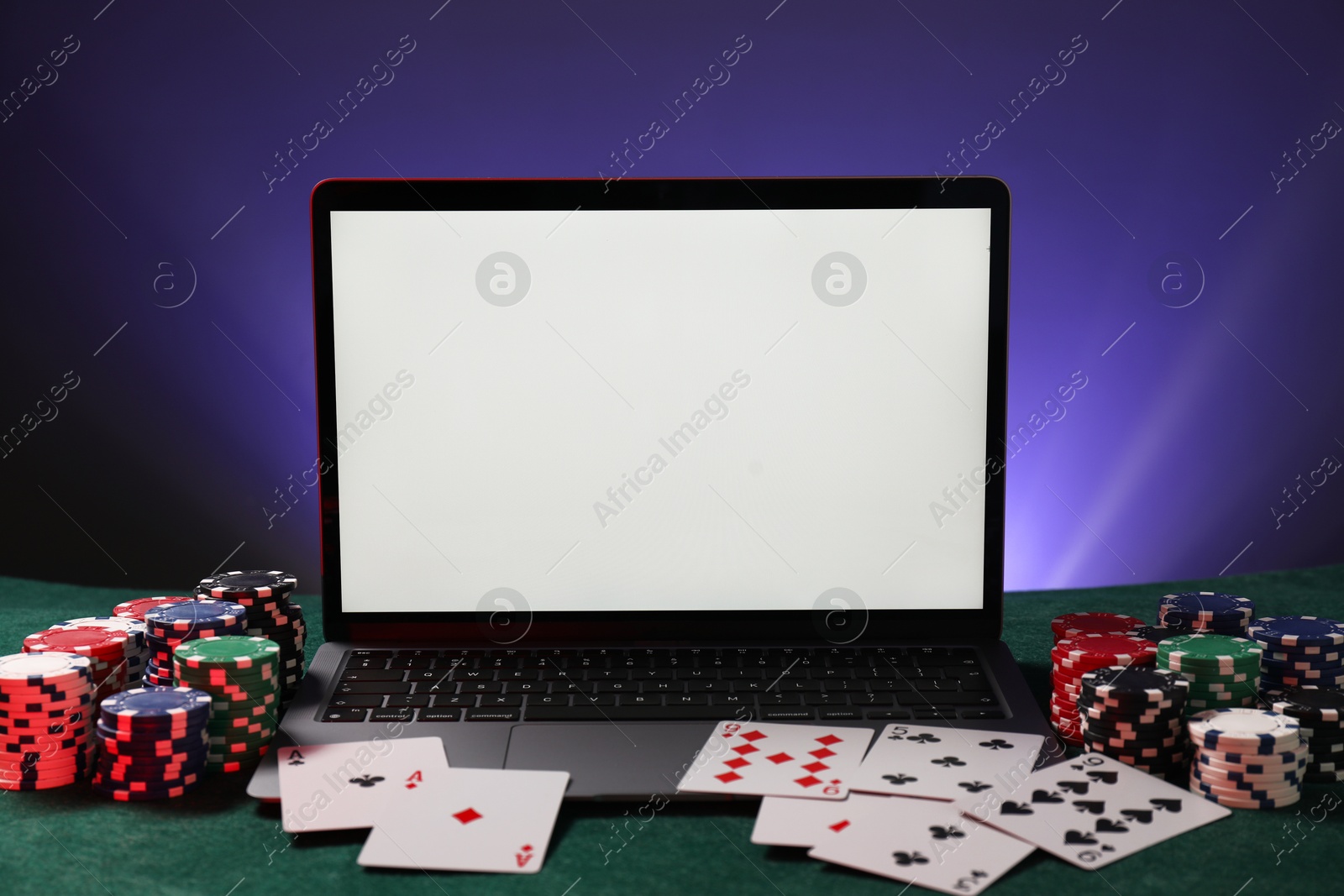 Photo of Laptop, poker chips and playing cards on green table. Online game