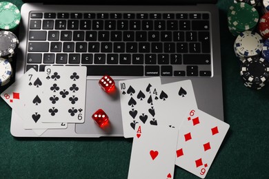 Photo of Laptop, poker chips, dices and playing cards on green table, above view. Online game