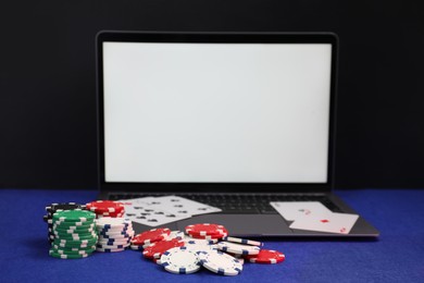 Photo of Laptop, poker chips and playing cards on blue table. Online game