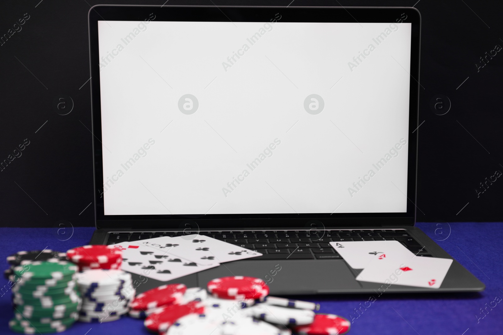 Photo of Laptop, poker chips and playing cards on blue table, closeup. Online game