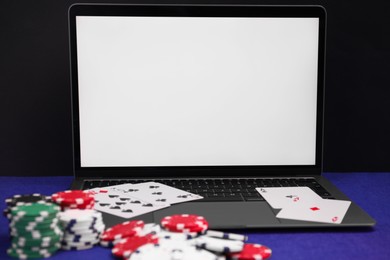 Photo of Laptop, poker chips and playing cards on blue table, closeup. Online game