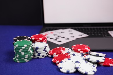 Photo of Laptop, poker chips and playing cards on blue table, closeup. Online game