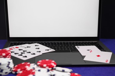 Photo of Laptop, poker chips and playing cards on blue table, closeup. Online game