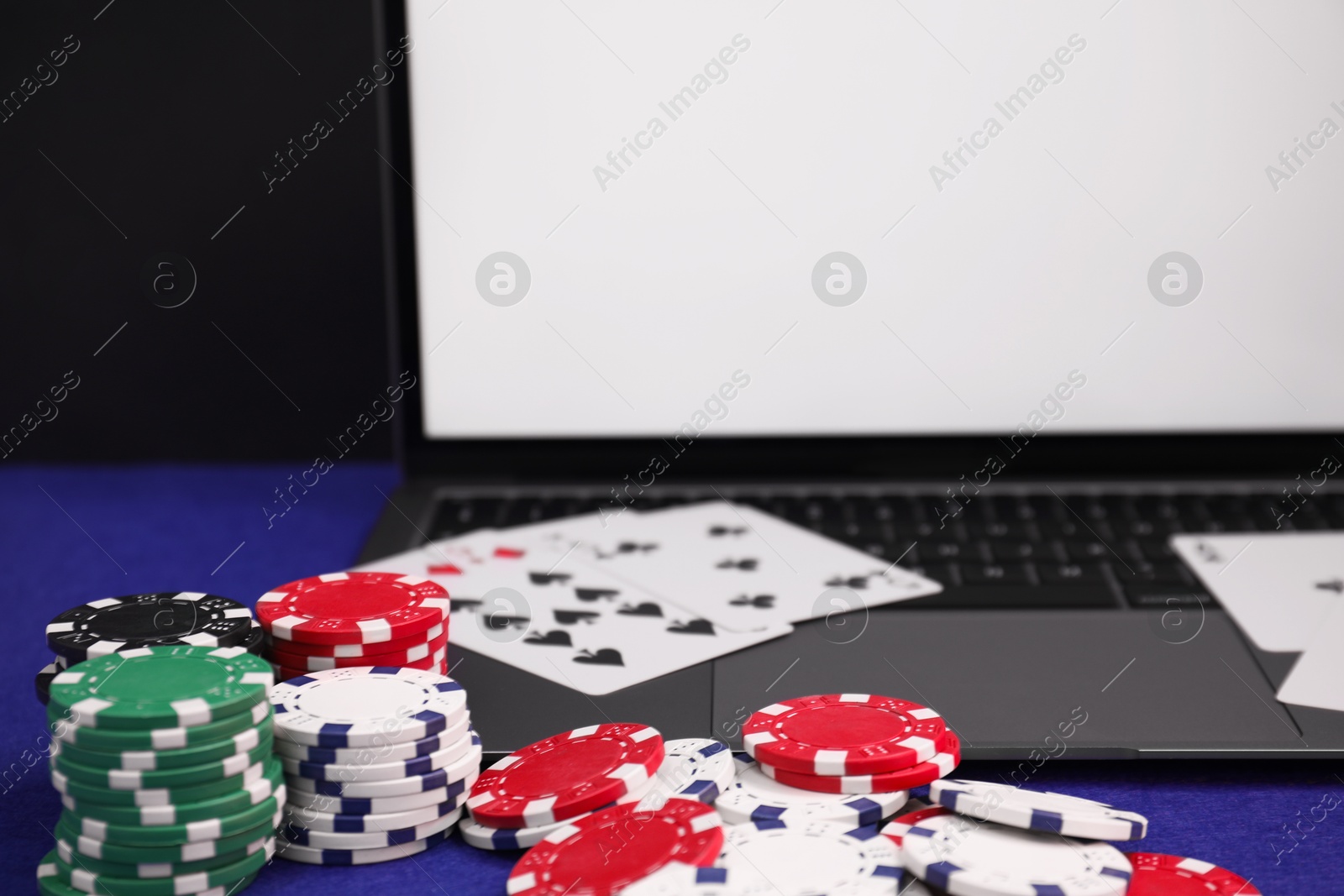 Photo of Laptop, poker chips and playing cards on blue table, closeup. Online game